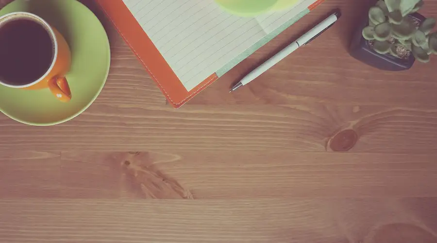 Kaffeetasse, Notizbuch und kleine Pflanze auf einem Holztisch