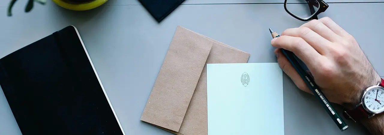 Schreibtisch mit Notizbuch, Tablet und schreibender Hand