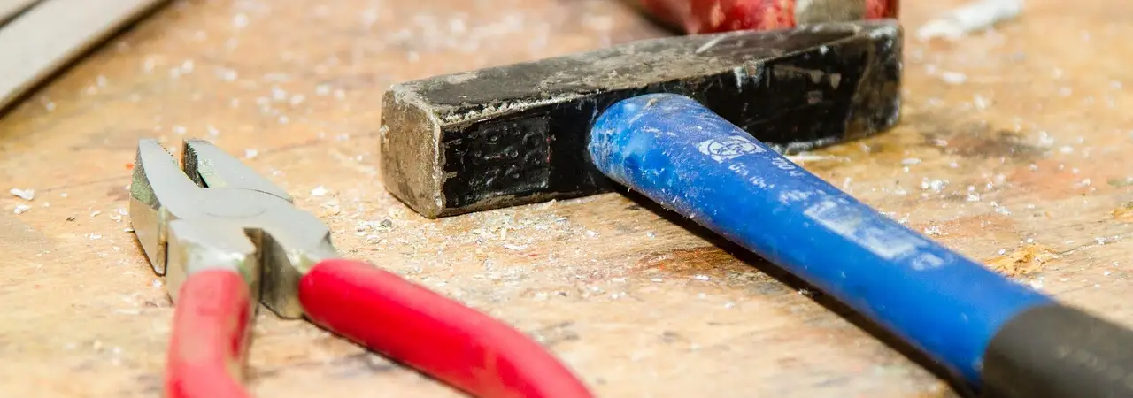Gebrauchte Werkzeuge wie Hammer und Zange liegen auf einer Werkbank