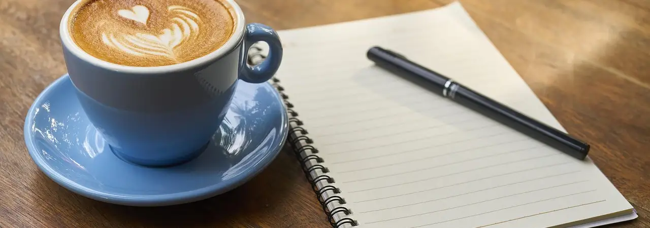 Kaffeetasse und aufgeschlagenes Notizbuch auf einem Holztisch
