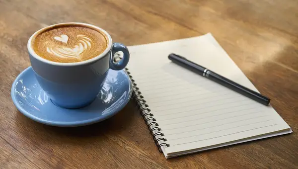 Kaffeetasse und aufgeschlagenes Notizbuch auf einem Holztisch