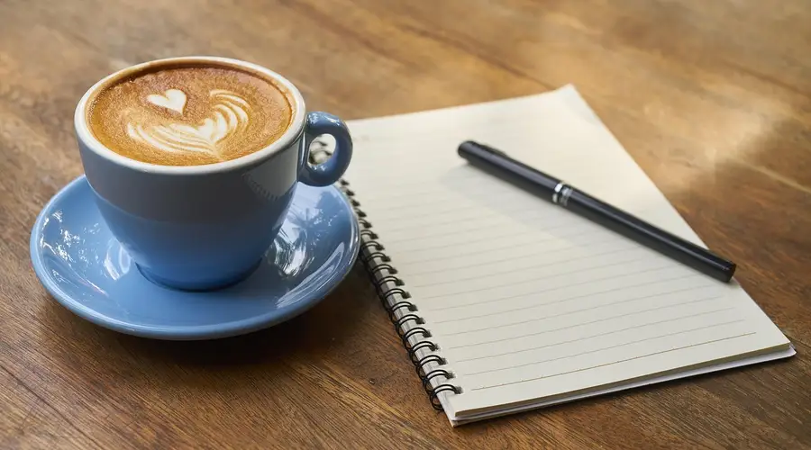 Kaffeetasse und aufgeschlagenes Notizbuch auf einem Holztisch
