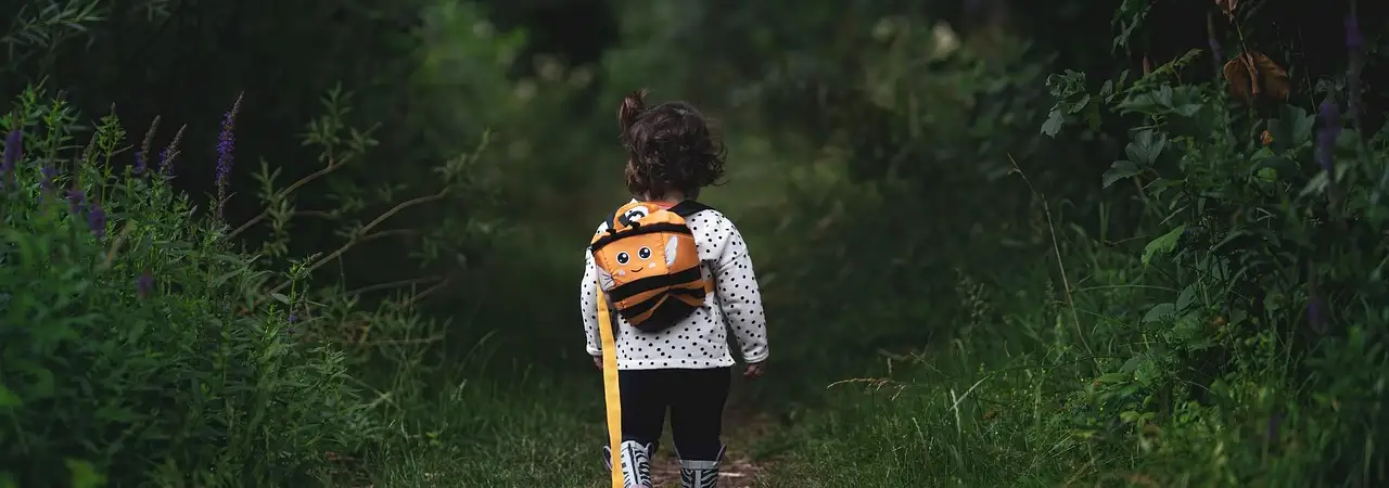 Kind mit Rucksack läuft allein einen grünen Waldweg entlang